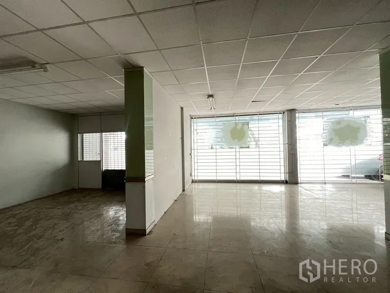 Shophouse for rent in Phra Khanong, Bangkok - Spacious ground-floor retail area with tiled floor, large glass frontage and security grilles.