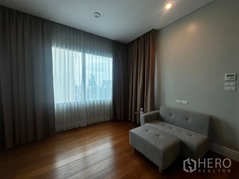 Condominium for rent in Khlong Toei, Bangkok - Cozy lounge corner with gray loveseat by a wide window overlooking the skyline.