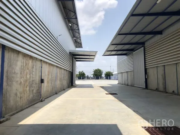 Factory for rent in Lat Lum Kaeo, Pathum Thani - Truck-friendly driveway between two metal-clad factory buildings with covered loading canopies.