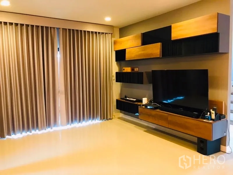 Detached House for rent or sale in Pathum Thani - Living room media wall with built-in shelves, large TV and full-height drapes.