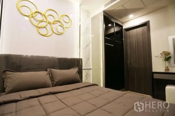 Condominium for rent in Watthana, Bangkok - Cozy bedroom with upholstered headboard, gold ring wall art and built-in storage.
