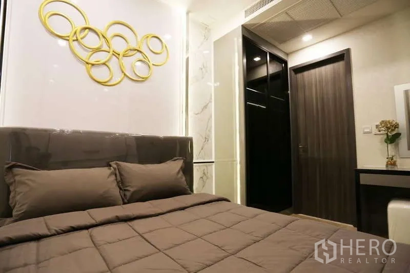 Condominium for rent in Watthana, Bangkok - Cozy bedroom with upholstered headboard, gold ring wall art and built-in storage.