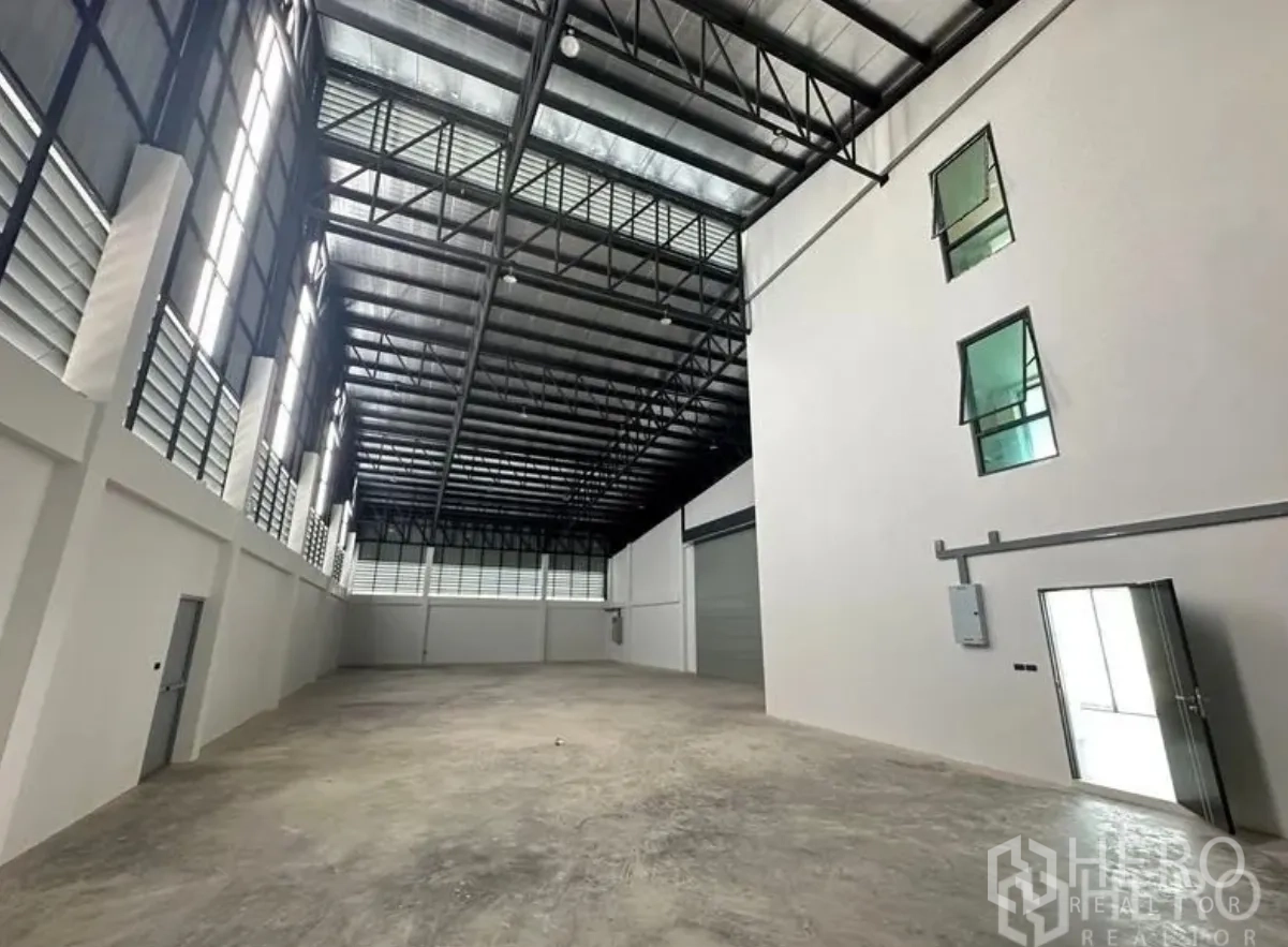 Warehouse for sale in Lam Luk Ka, Pathum Thani - Wide warehouse hall featuring ventilated side panels, steel roof trusses and a large roller door.