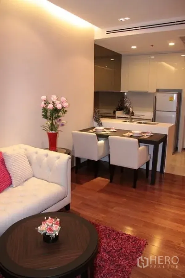 Condominium for rent in Khlong Toei, Bangkok - Compact living room with sofa and round coffee table beside the dining area and kitchen.