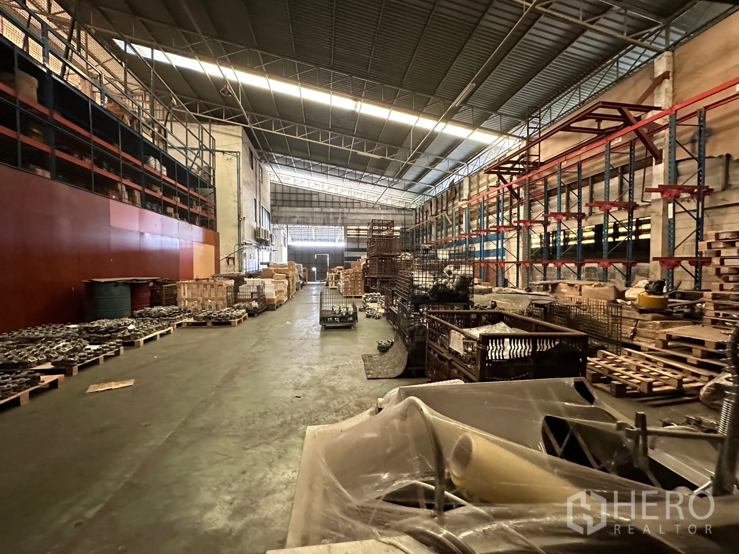 Factory for rent in Lam Luk Ka, Pathum Thani - Long warehouse aisle with racking systems and stacked pallets in an industrial hall.