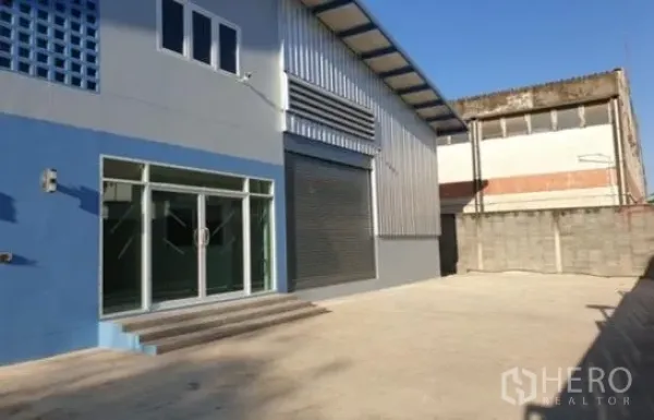 Warehouse for rent in Prawet, Bangkok - Gated warehouse exterior with glass-front office, roller shutter and wide concrete yard.