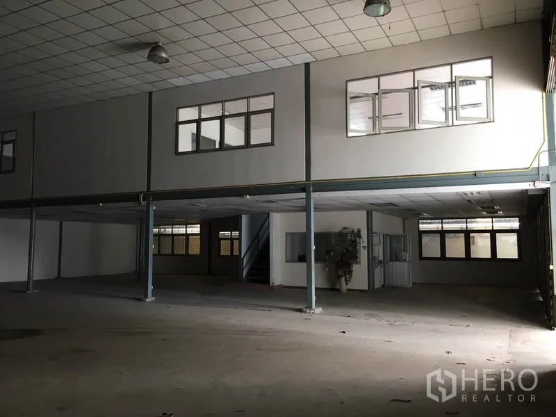 Warehouse for rent in Prawet, Bangkok - Spacious warehouse interior with high ceiling, steel columns, pendant lights and mezzanine offices with windows and stairs.