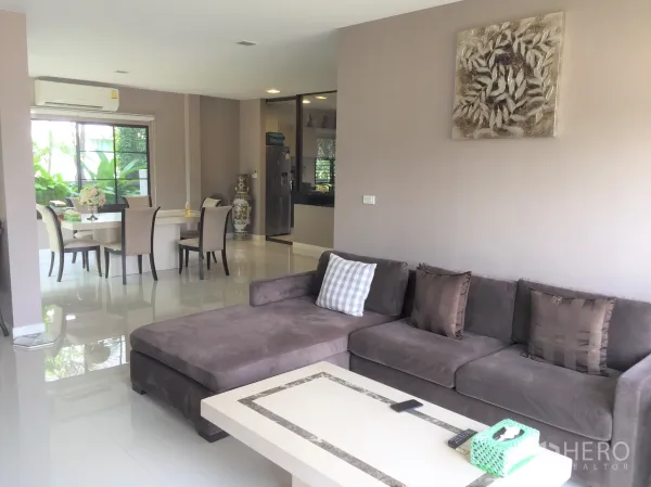 Detached House for rent or sale in Prawet, Bangkok - Bright open-plan living and dining area with L-shaped sofa, glossy tile floors and large garden-facing windows.