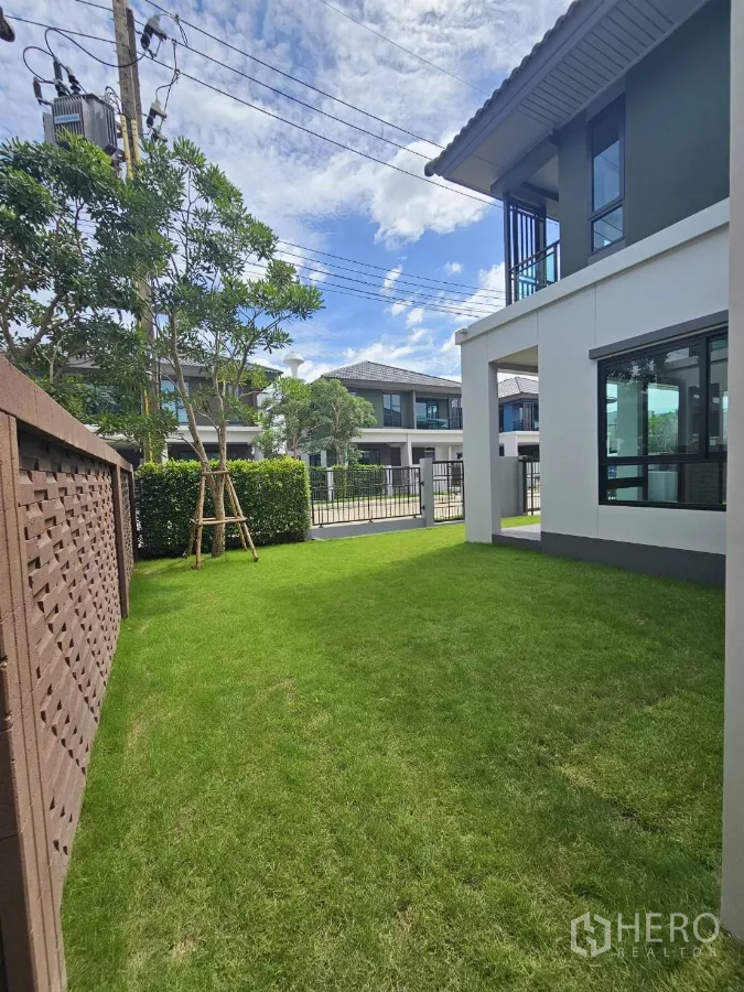 Detached House for sale in Lam Luk Ka, Pathum Thani - Front garden lawn facing the street and gated entrance.