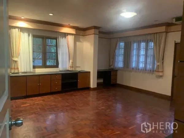 Detached House for rent in Khan Na Yao, Bangkok - Spacious multipurpose room with parquet flooring, corner windows with sheer curtains, and built-in cabinetry.