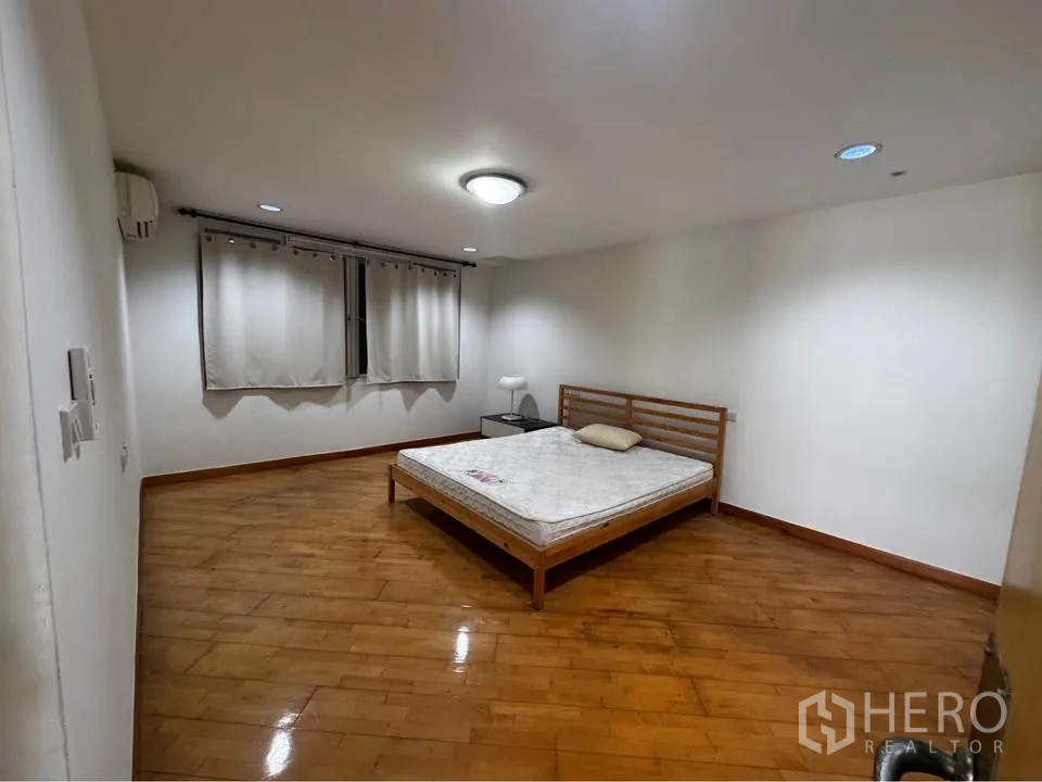 Townhouse for rent in Huai Khwang, Bangkok - Simple bedroom with bed, nightstand and polished wooden floor.