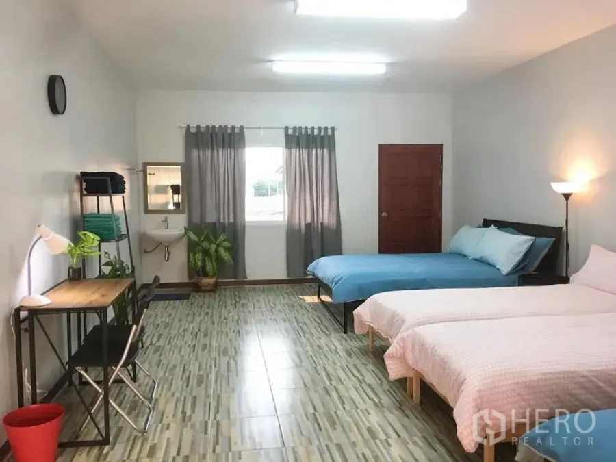 Townhouse for rent in Bang Rak, Bangkok - Spacious bedroom with three beds, study desk, tiled floor, curtained window and a potted plant.