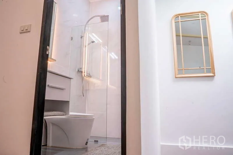 Townhouse for rent in Khlong Toei, Bangkok - Bathroom with glass shower enclosure, vanity and illuminated mirror.