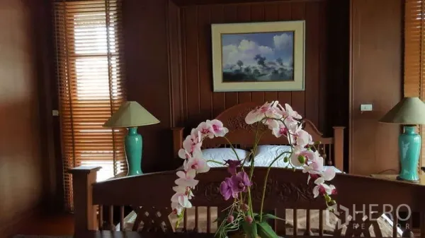 Townhouse for rent in Khlong Toei, Bangkok - Master bedroom with carved wooden bed, wood panel walls and bedside lamps.